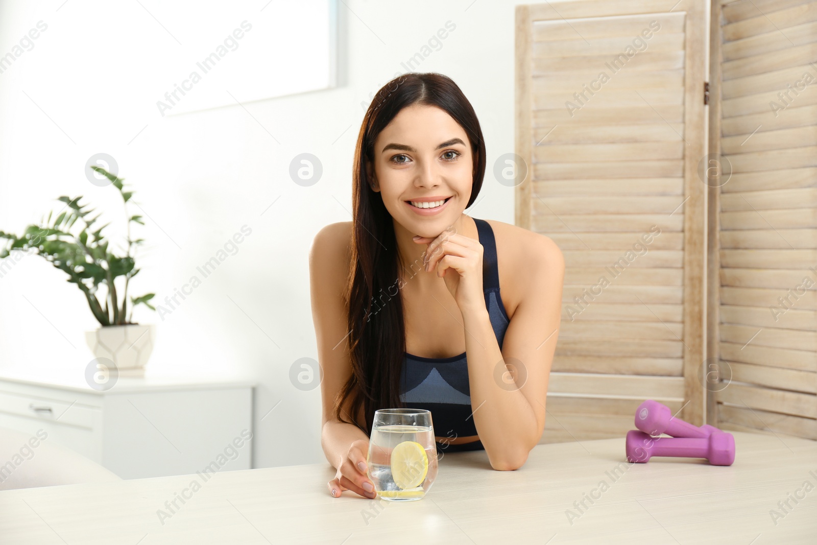 Photo of Beautiful sportive woman with lemon water at table indoors