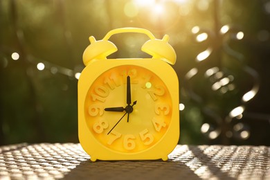 Photo of Yellow alarm clock on table outdoors at sunny morning