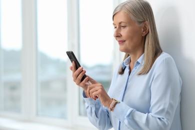 Senior woman using mobile phone at home, space for text