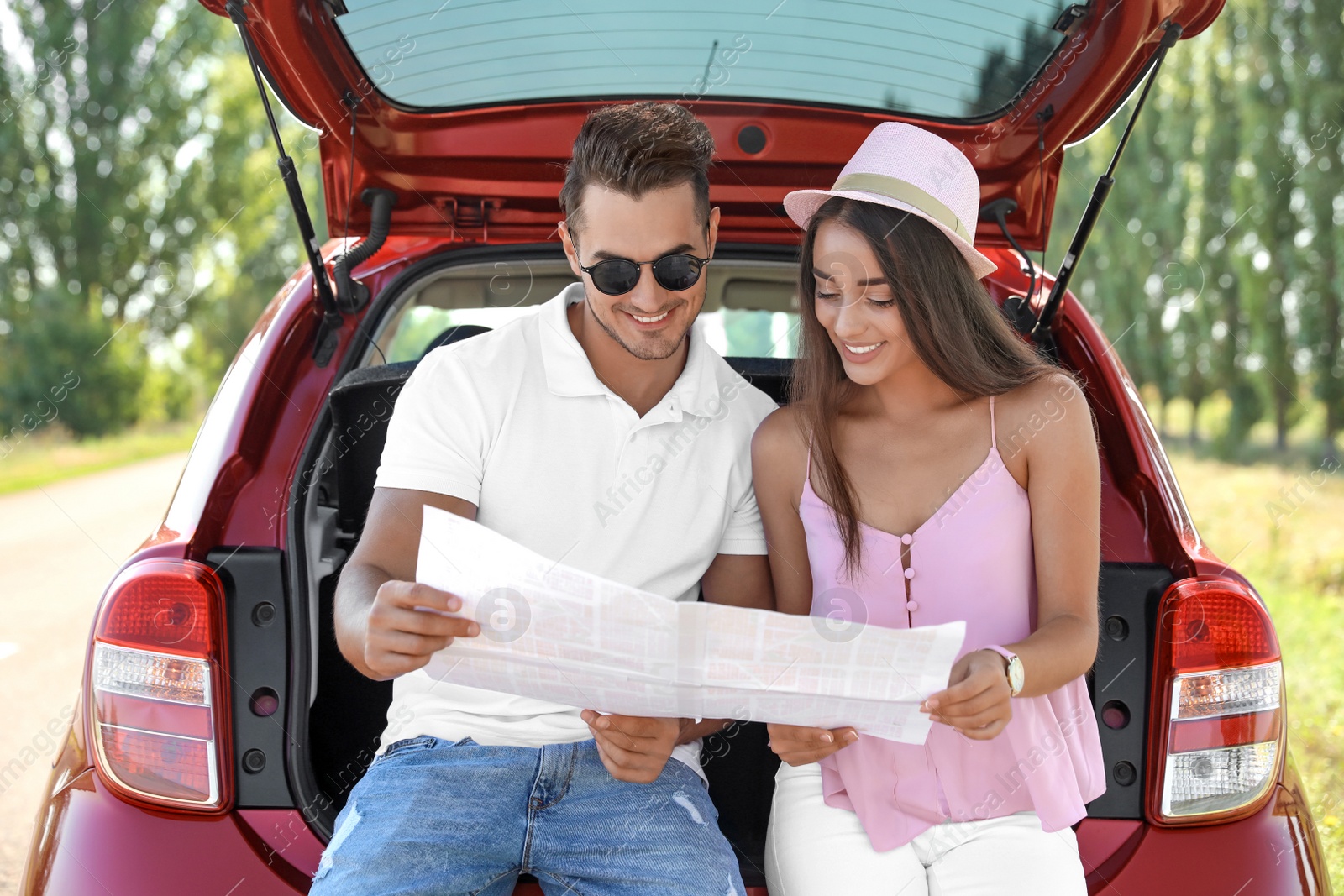 Photo of Young couple with map sitting in open car trunk outdoors