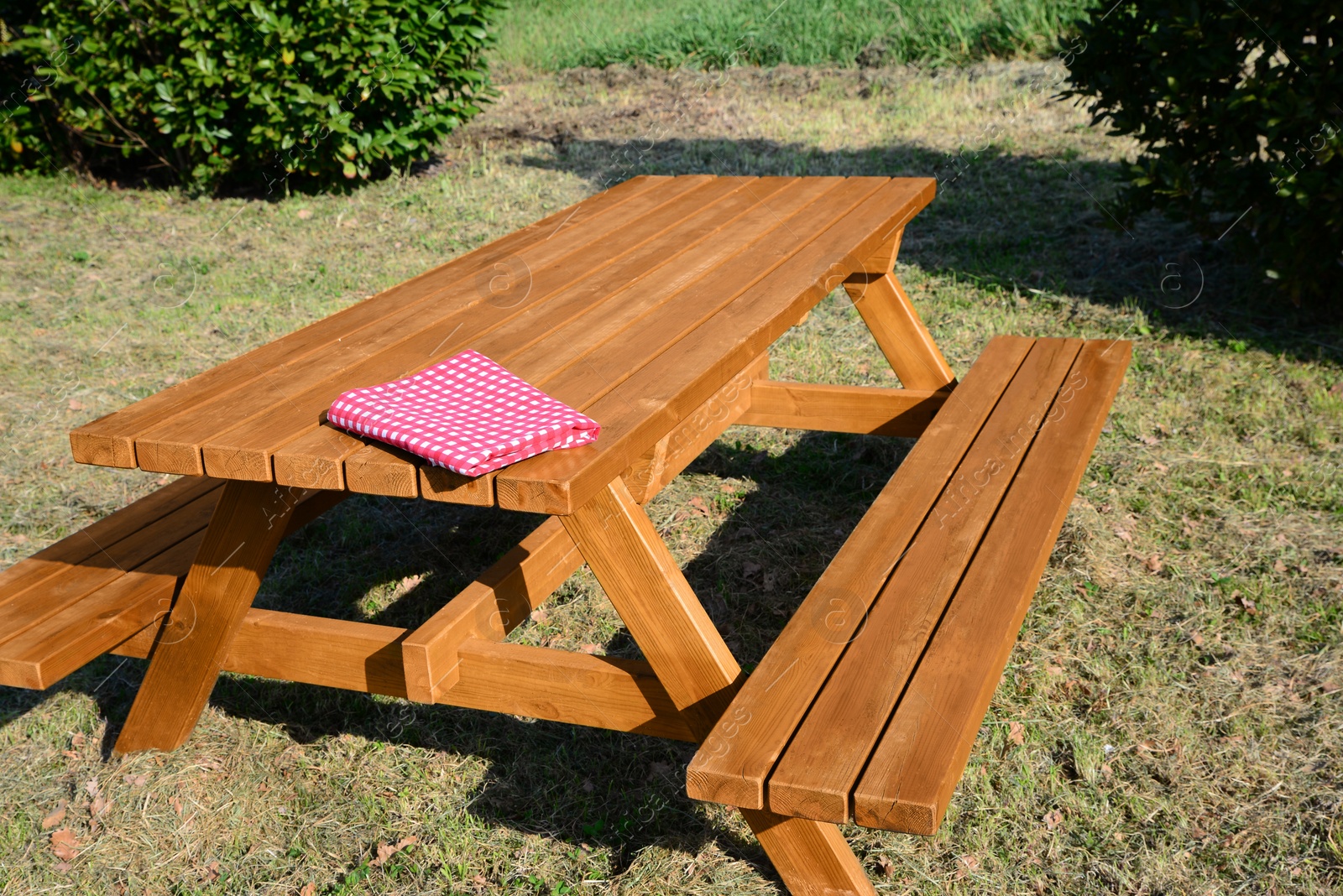 Photo of Folded red and white checkered tablecloth on wooden picnic table in park