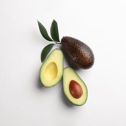 Whole and cut ripe avocadoes with green leaves on white background, top view