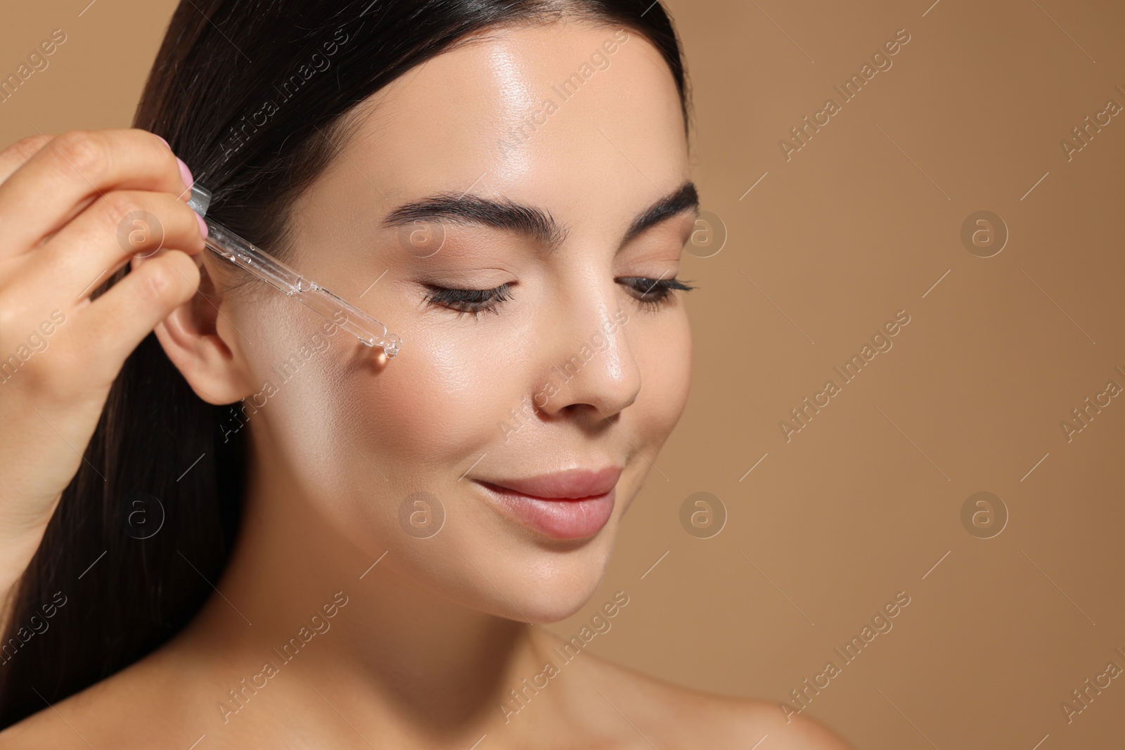 Photo of Beautiful young woman applying serum onto her face on beige background, closeup. Space for text