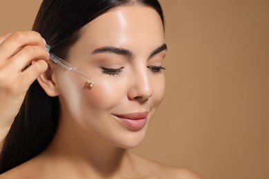 Beautiful young woman applying serum onto her face on beige background, closeup. Space for text