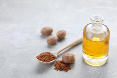 Photo of Bottle of nutmeg oil, nuts and powder on light grey table, closeup. Space for text