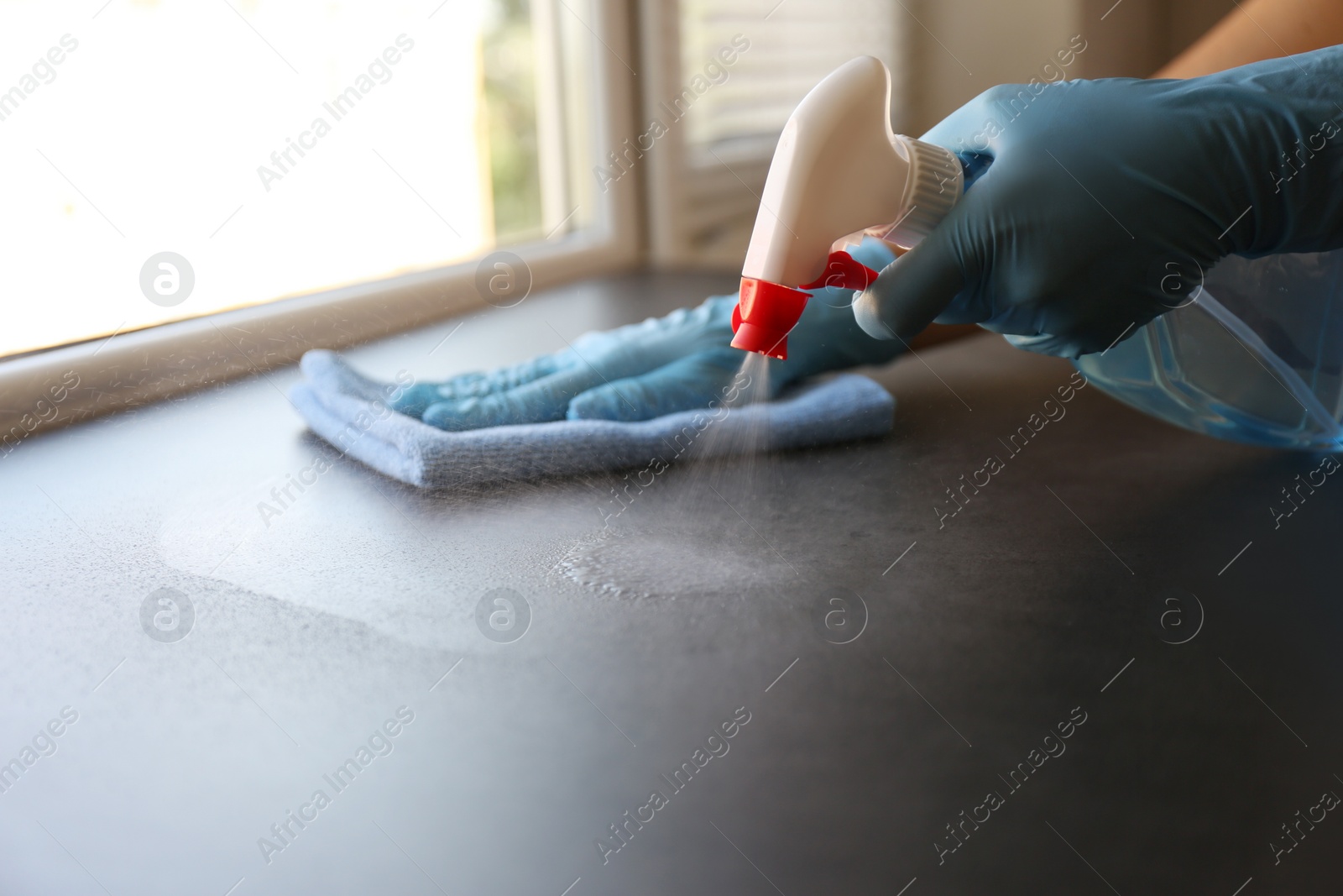 Photo of Woman in gloves cleaning grey window sill with rag and detergent indoors, closeup