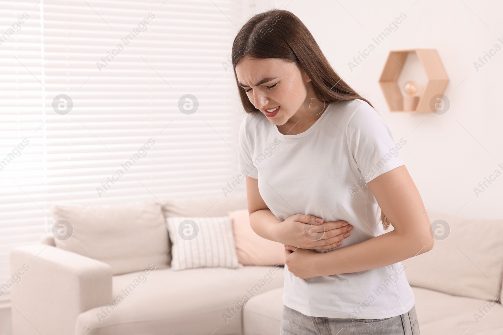 Photo of Young woman suffering from stomach pain at home. Space for text