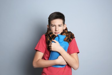 Photo of Sick teenage boy with hot water bottle on grey background