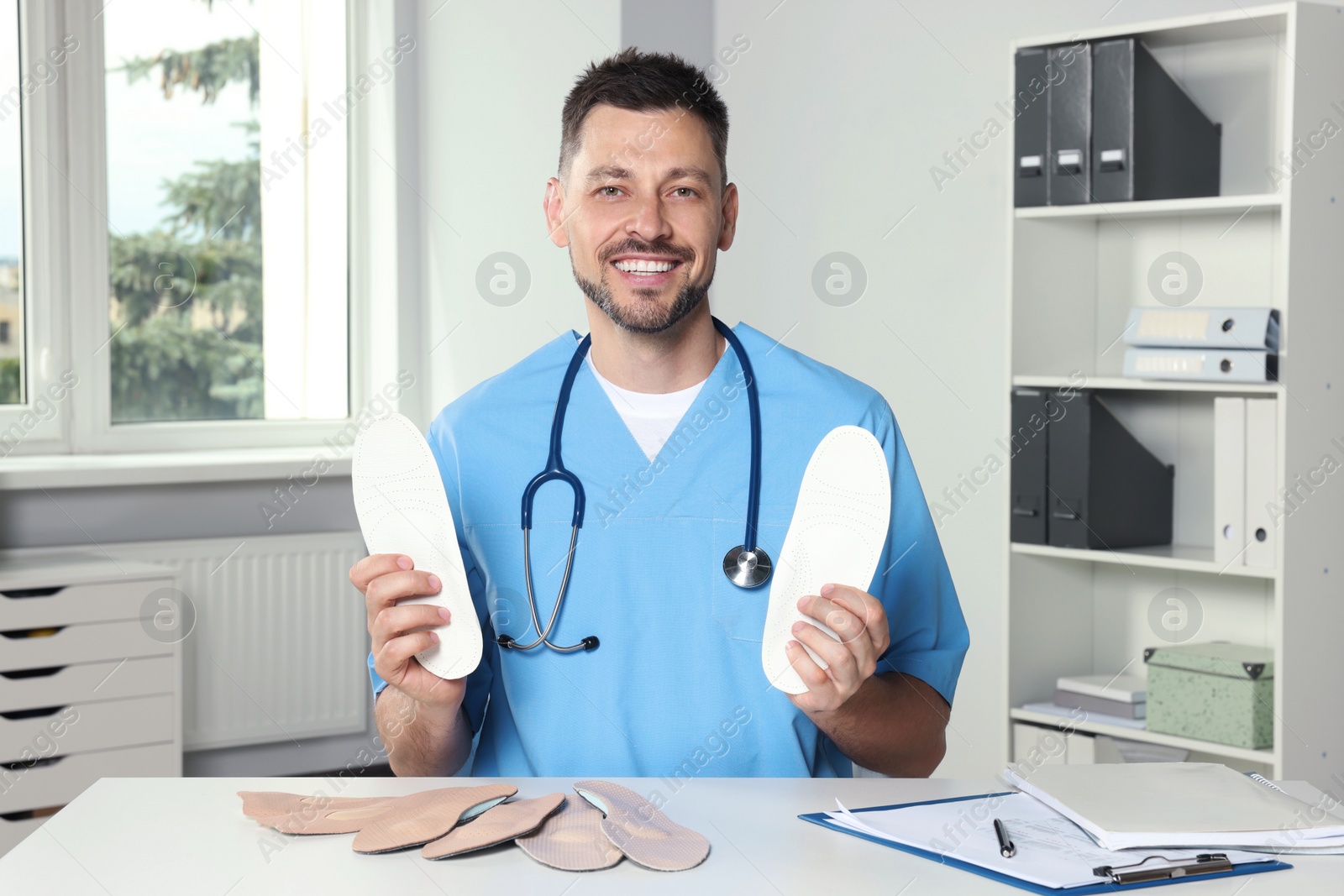 Photo of Handsome male orthopedist showing insoles in hospital