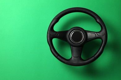 Photo of New black steering wheel on green background, space for text