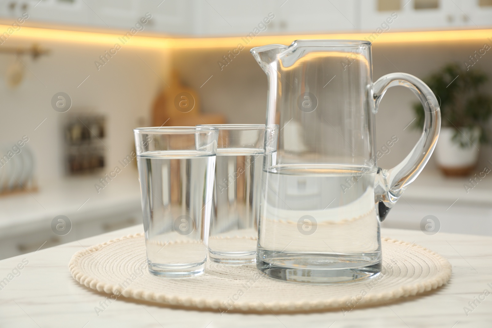 Photo of Jug and glasses with clear water on white table in kitchen