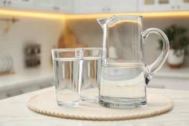 Jug and glasses with clear water on white table in kitchen