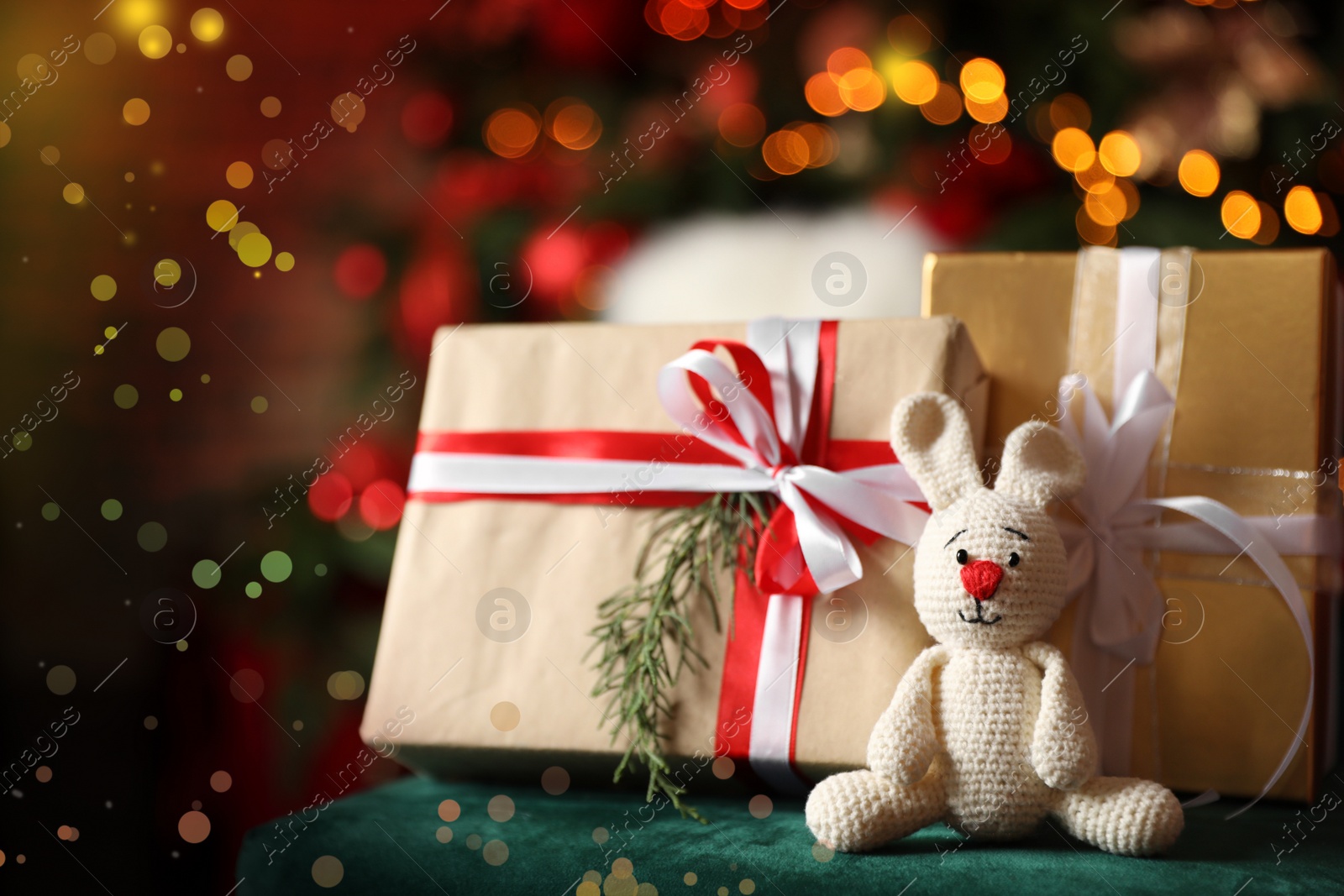 Photo of Christmas gifts and bunny on table against blurred festive lights