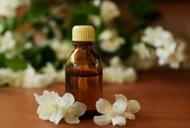 Photo of Bottle of jasmine essential oil and beautiful flowers on wooden table, closeup