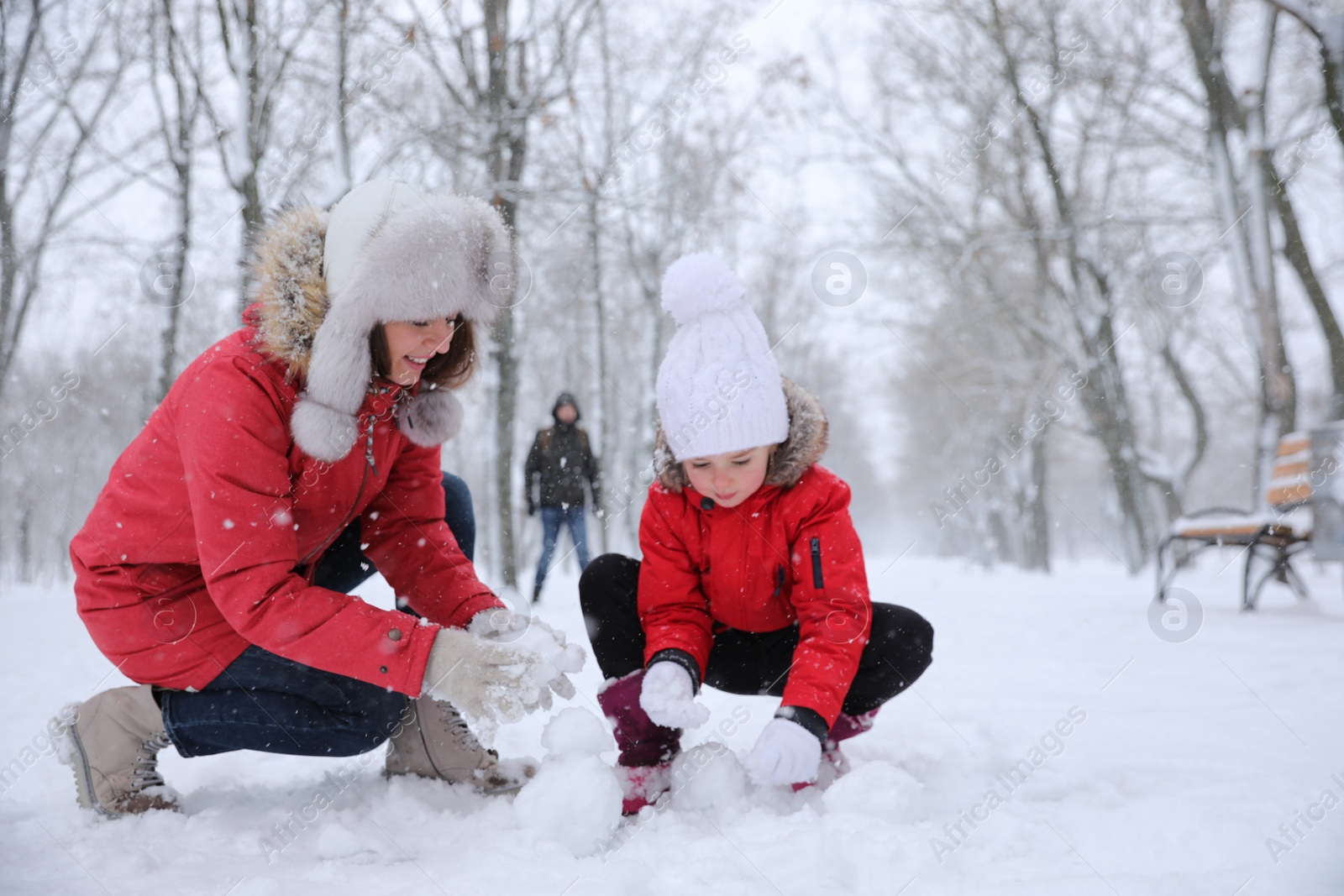 Photo of Mother with her child building small snowman outside on winter day. Christmas vacation