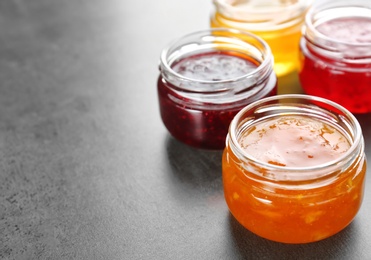Jars with different sweet jam on grey background