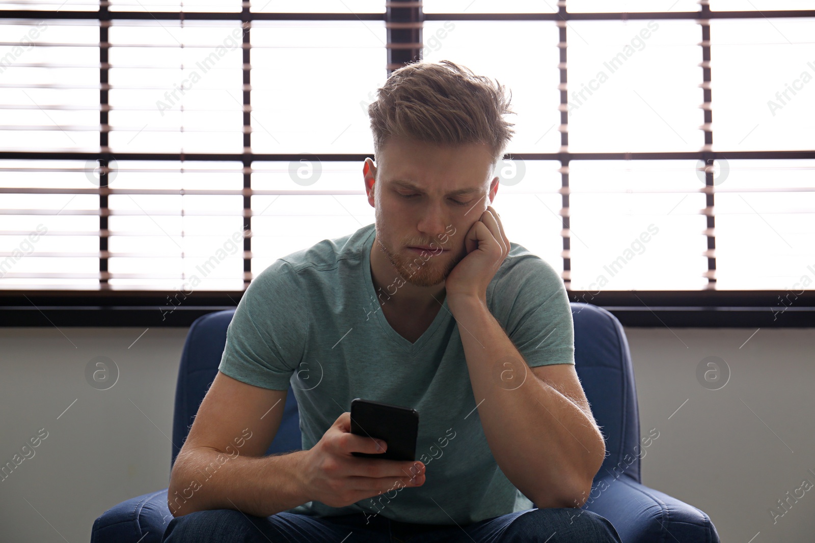 Photo of Lonely man with mobile phone in armchair near window indoors