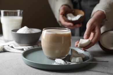 Woman putting coconut pieces near glass of coffee with milk, closeup