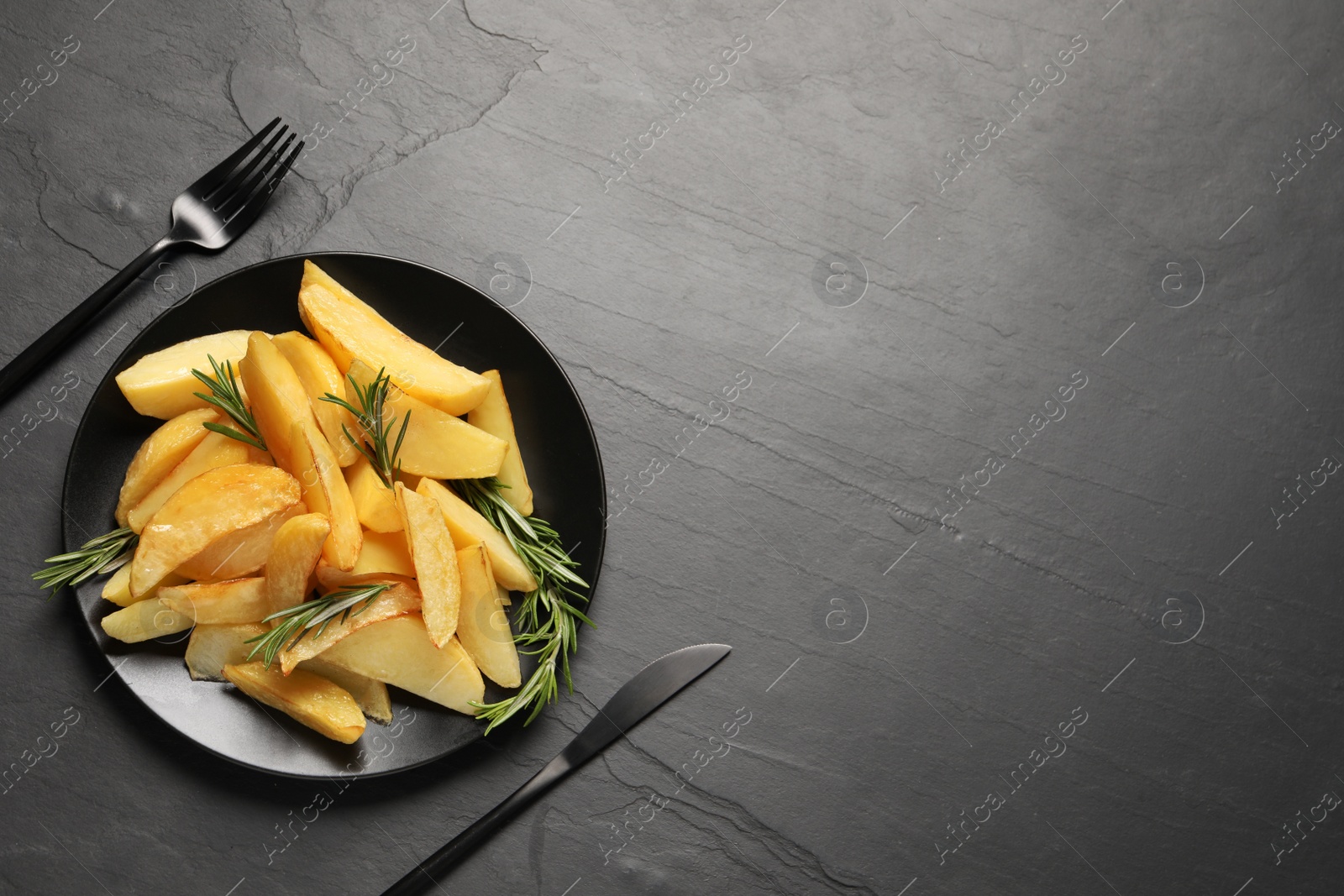 Photo of Served tasty baked potato wedges and rosemary on black table, flat lay. Space for text