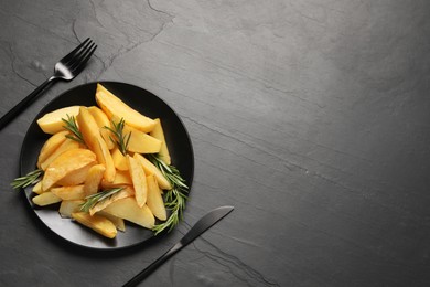 Photo of Served tasty baked potato wedges and rosemary on black table, flat lay. Space for text
