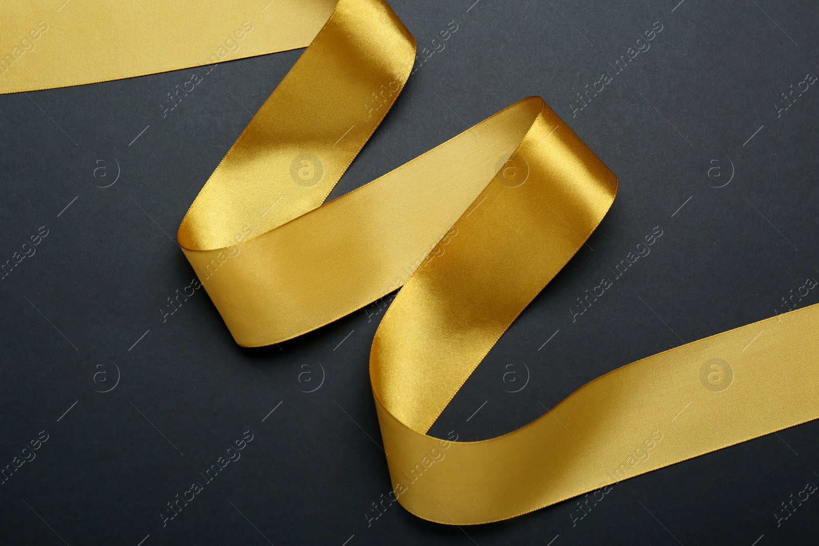 Photo of Beautiful golden ribbon on black background, top view