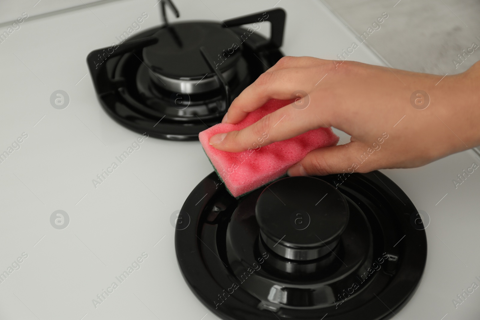 Photo of Woman cleaning gas stove with sponge, closeup