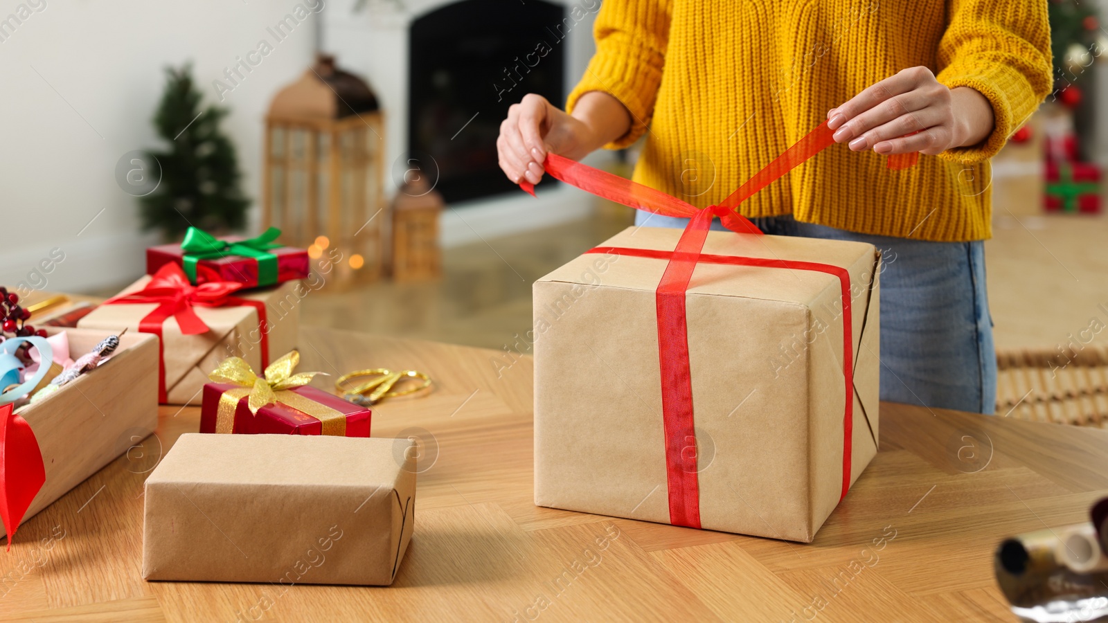 Photo of Woman wrapping Christmas gift at wooden table indoors, closeup