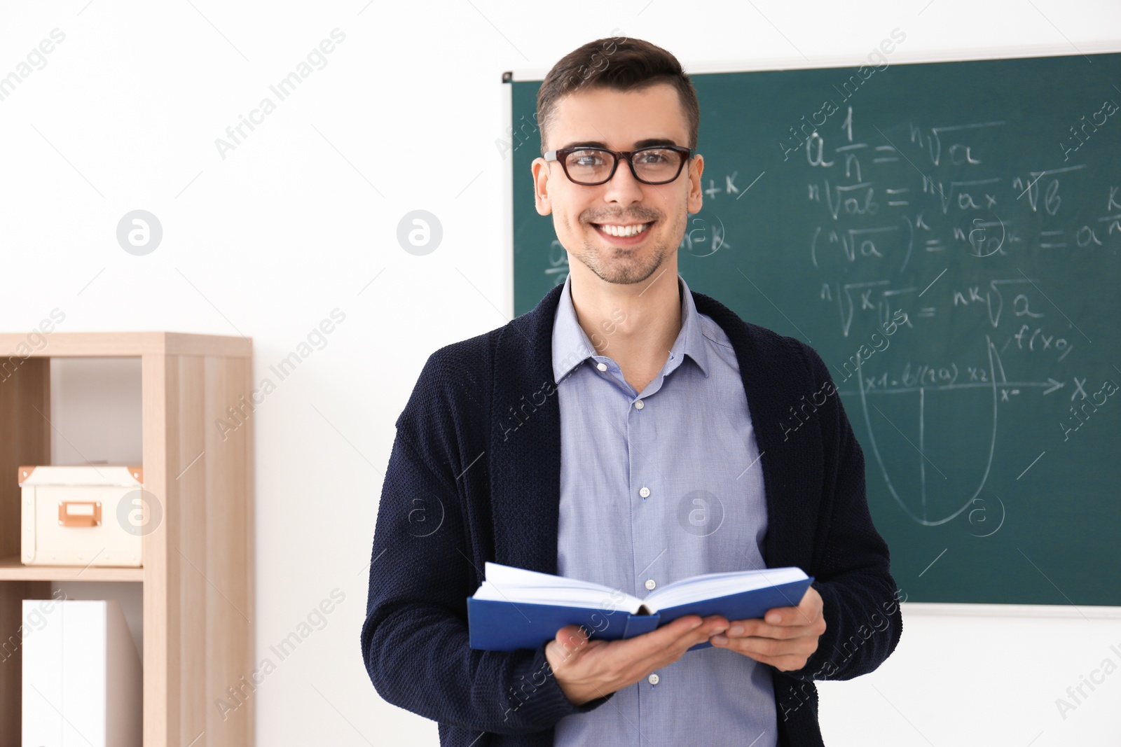 Photo of Young male teacher with book standing in classroom