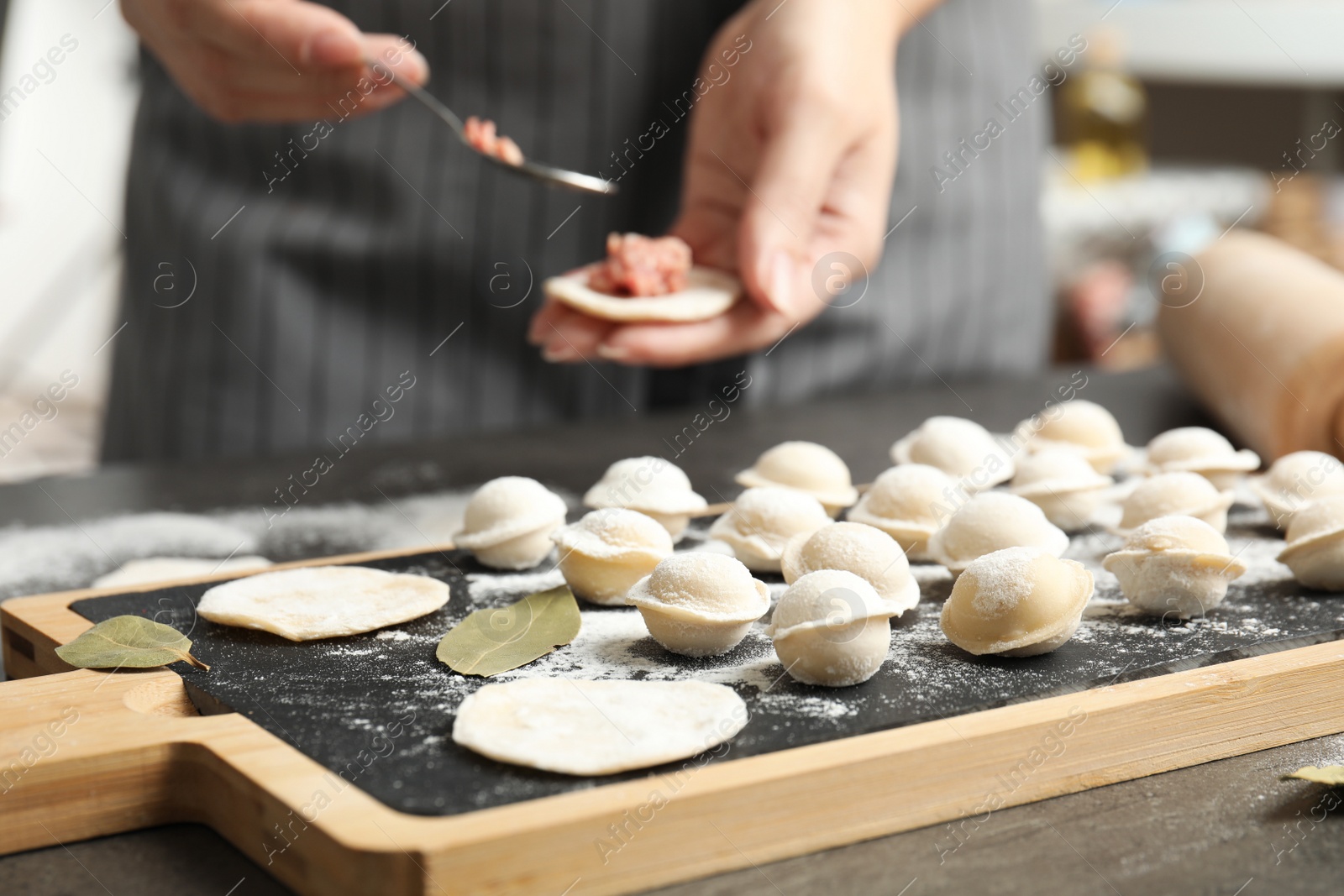 Photo of Woman cooking delicious dumplings over grey table, closeup