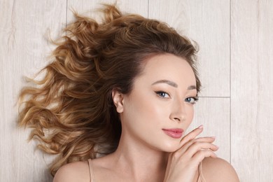 Photo of Portrait of beautiful woman with curly hair on wooden floor, top view