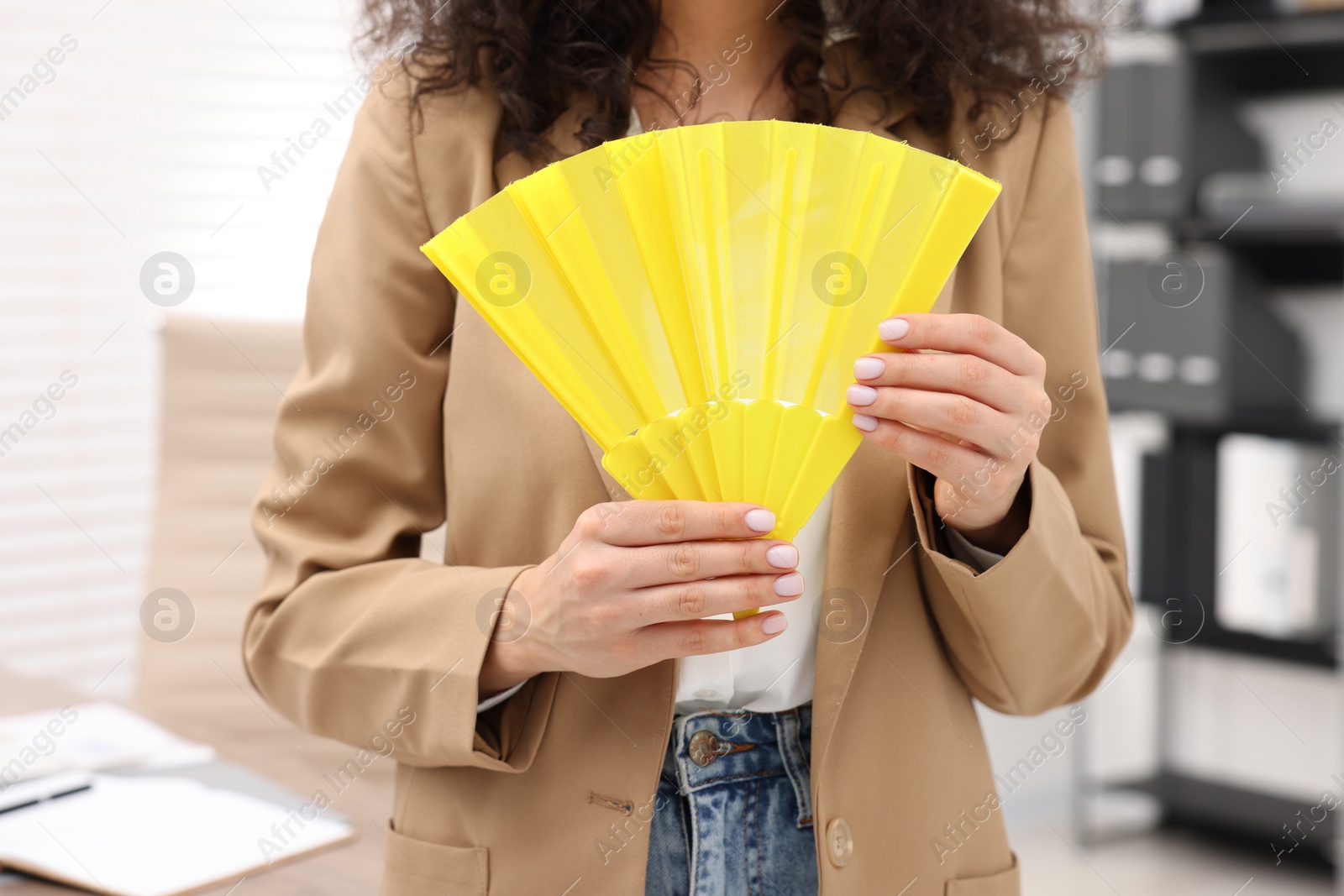 Photo of Woman with yellow hand fan in office, closeup