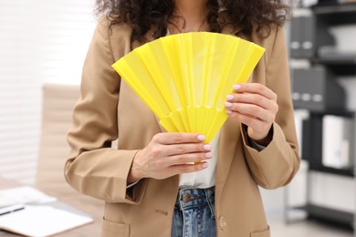 Woman with yellow hand fan in office, closeup