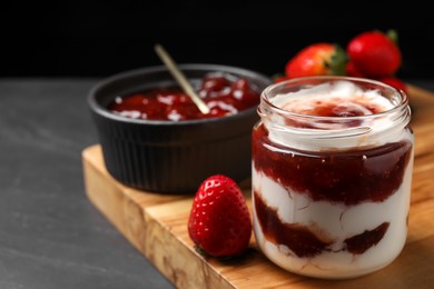 Photo of Tasty yoghurt with jam and strawberries on black table, closeup