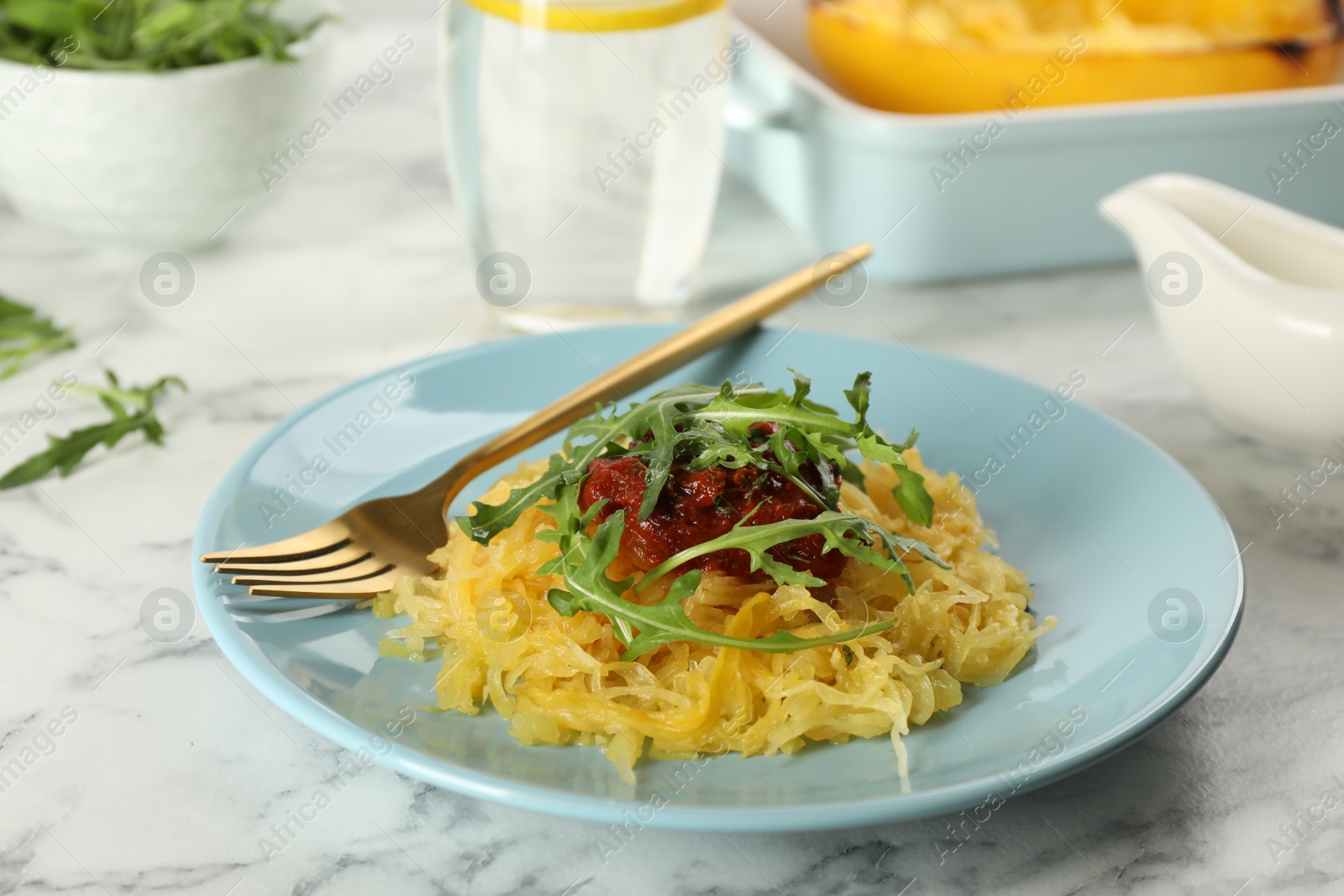 Photo of Tasty spaghetti squash with tomato sauce and arugula served on white marble table, closeup