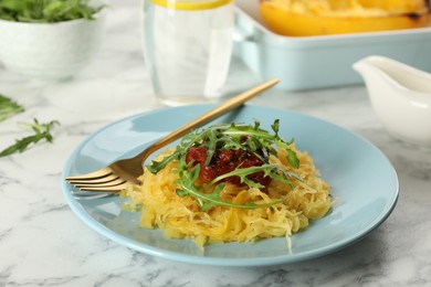 Photo of Tasty spaghetti squash with tomato sauce and arugula served on white marble table, closeup