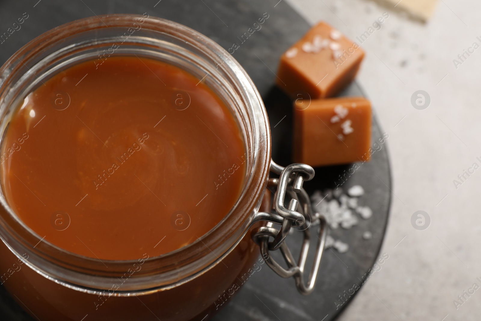 Photo of Tasty salted caramel in glass jar on grey table, closeup. Space for text