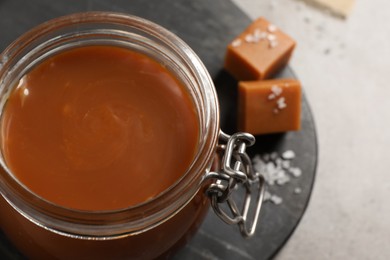 Tasty salted caramel in glass jar on grey table, closeup. Space for text