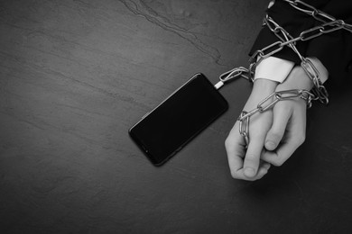 Top view of internet addicted woman chained to smartphone at dark table, space for text. Black and white effect