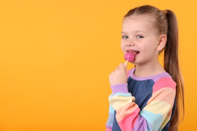 Photo of Cute little girl licking lollipop on orange background, space for text