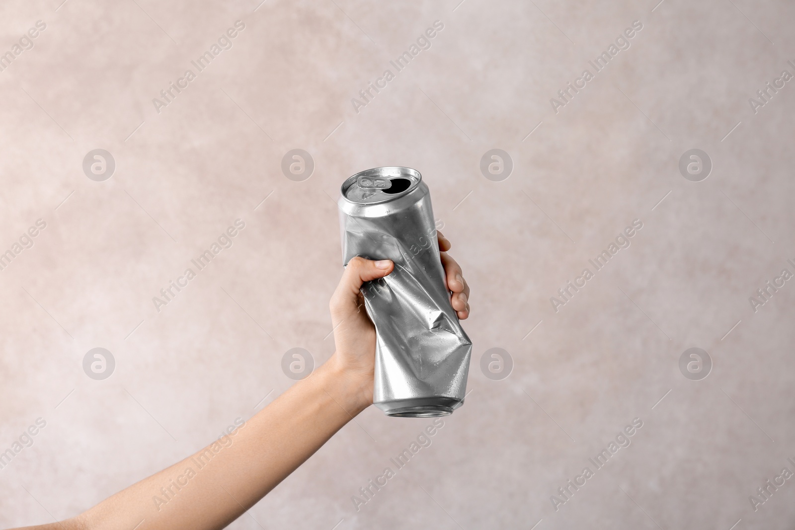 Photo of Woman holding crumpled aluminum can on light background. Metal waste recycling