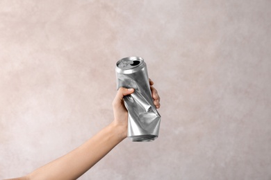 Woman holding crumpled aluminum can on light background. Metal waste recycling