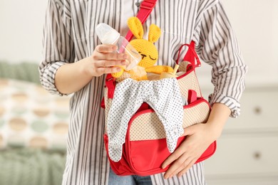 Photo of Woman putting baby`s bottle into mother`s bag indoors, closeup