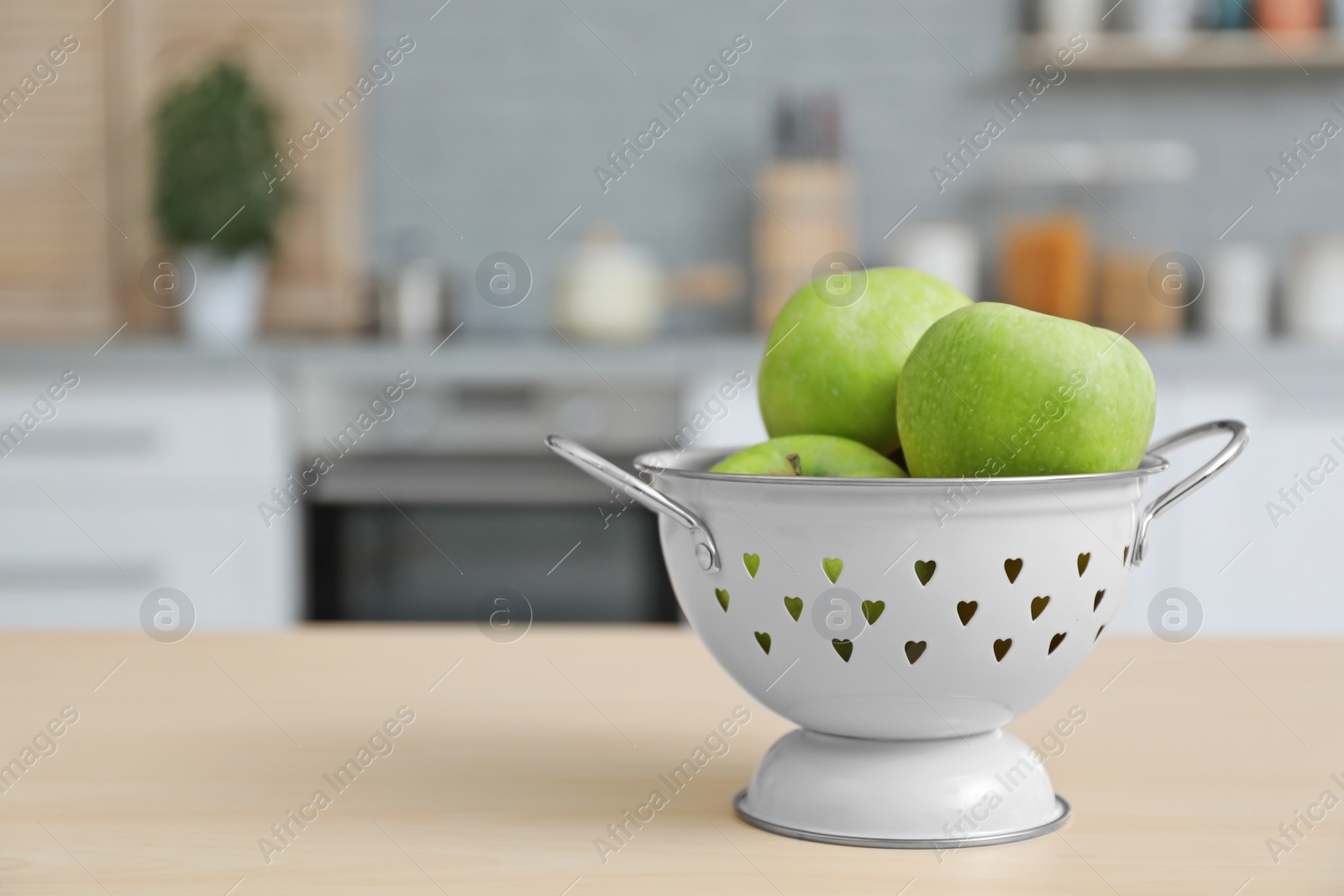 Photo of Ripe apples in colander and blurred view of kitchen interior on background