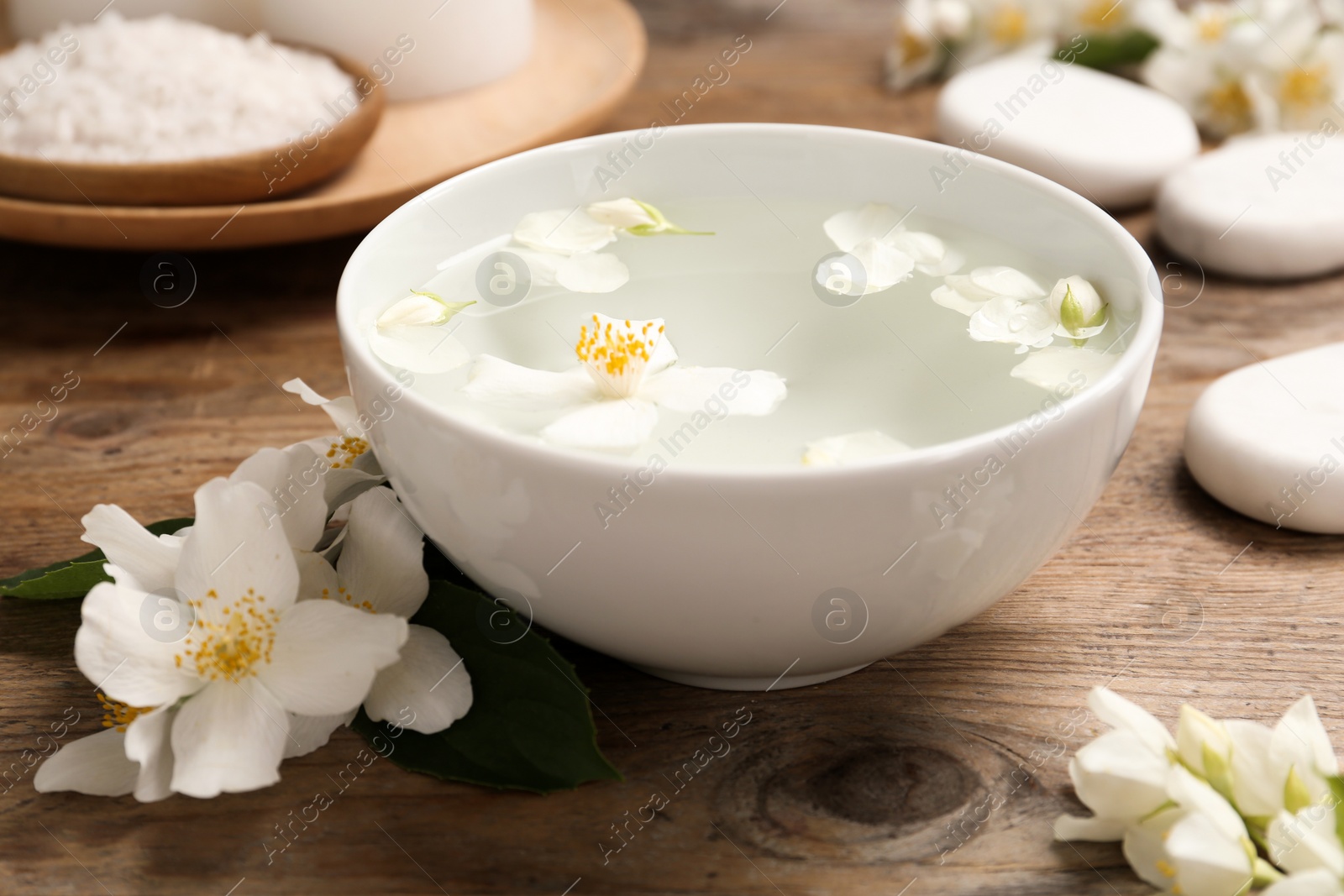 Photo of Bowl with water and beautiful jasmine flowers on wooden table