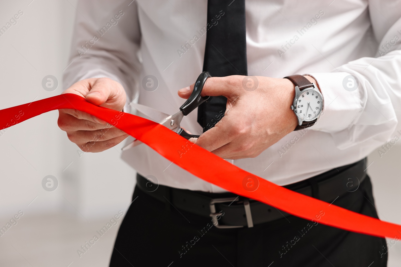 Photo of Man cutting red ribbon with scissors on blurred background, closeup