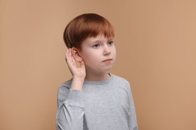 Little boy with hearing problem on pale brown background