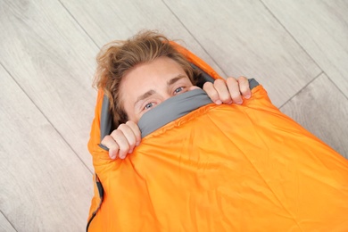 Young man in comfortable sleeping bag on floor, top view