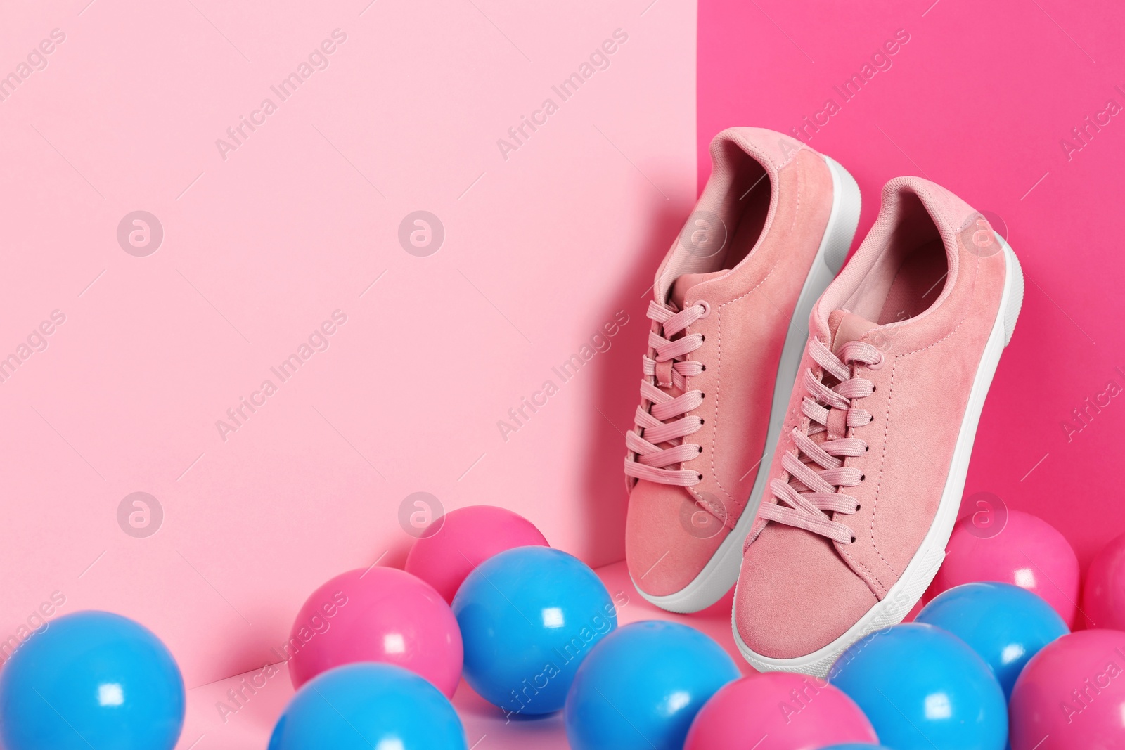 Photo of Comfortable sneakers and plastic balls on color background, space for text