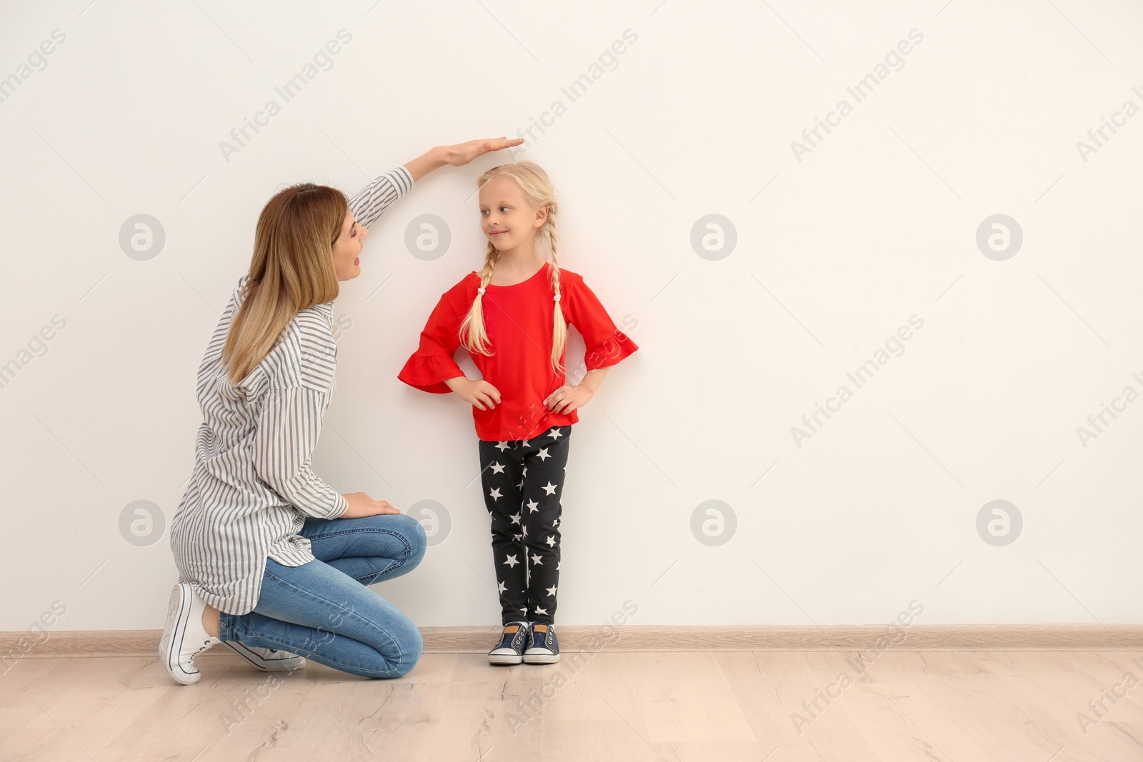 Photo of Young woman measuring her daughter's height indoors