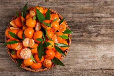 Fresh ripe juicy tangerines and green leaves on wooden table, top view. Space for text